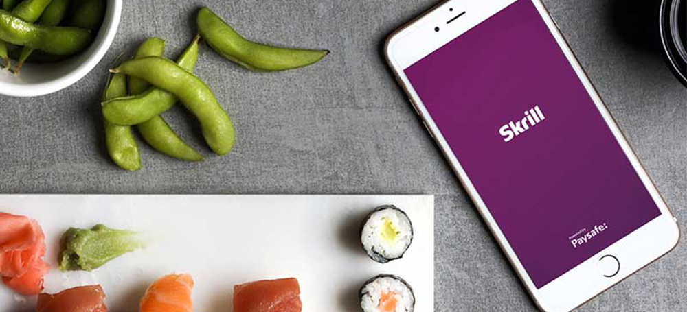 mobile phone with open Skrill app next to sushi set