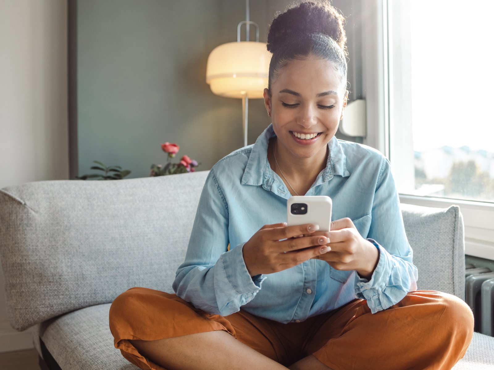woman sitting on a couch looking at her phone smiling